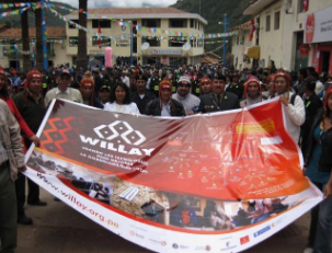 Un grupo numeroso de pobladores sostiene un banner del programa Willay durante una actividad pública en la plaza de un pueblo andino