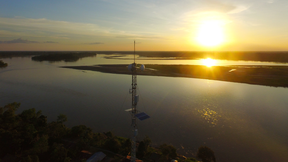 Torre de telecomunicaciones con antenas y panel solar sobre la selva, con el río Napo y el atardecer al fondo